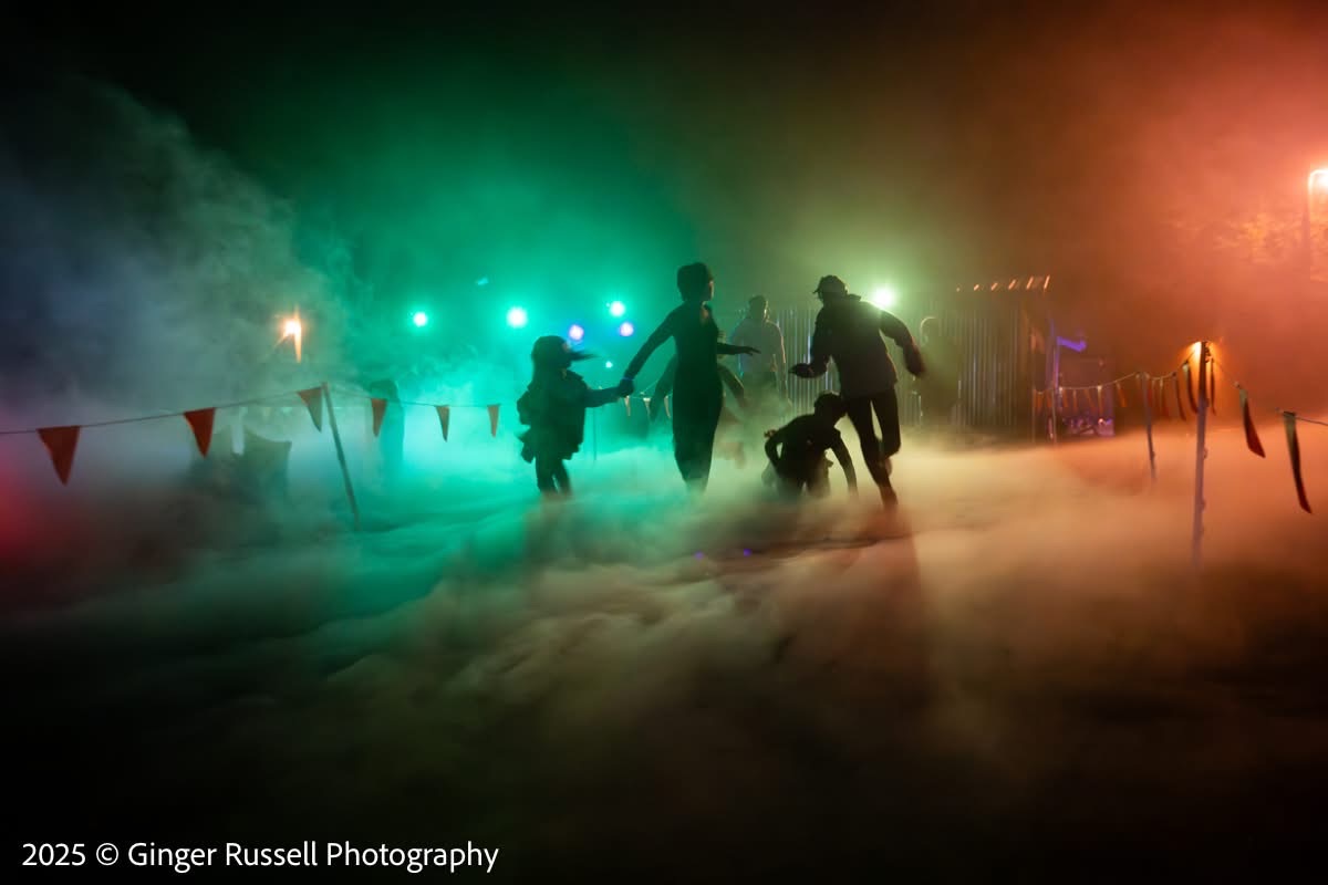 Silhouetted guests running through green fog toward the haunted house at night