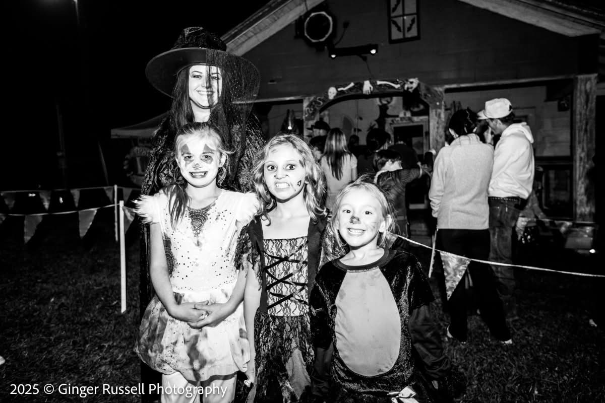 Black and white photo of a witch character posing with three costumed girls
