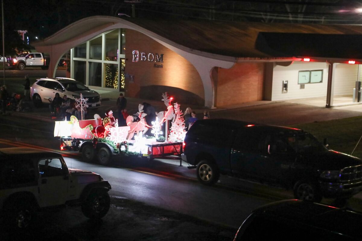 A lighted Santa sleigh float towed past a downtown Hemphill building during the Christmas Parade at night