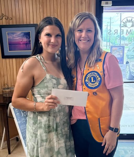 A Hemphill Lions Club member in a gold vest handing an envelope to a young woman inside a local Hemphill business
